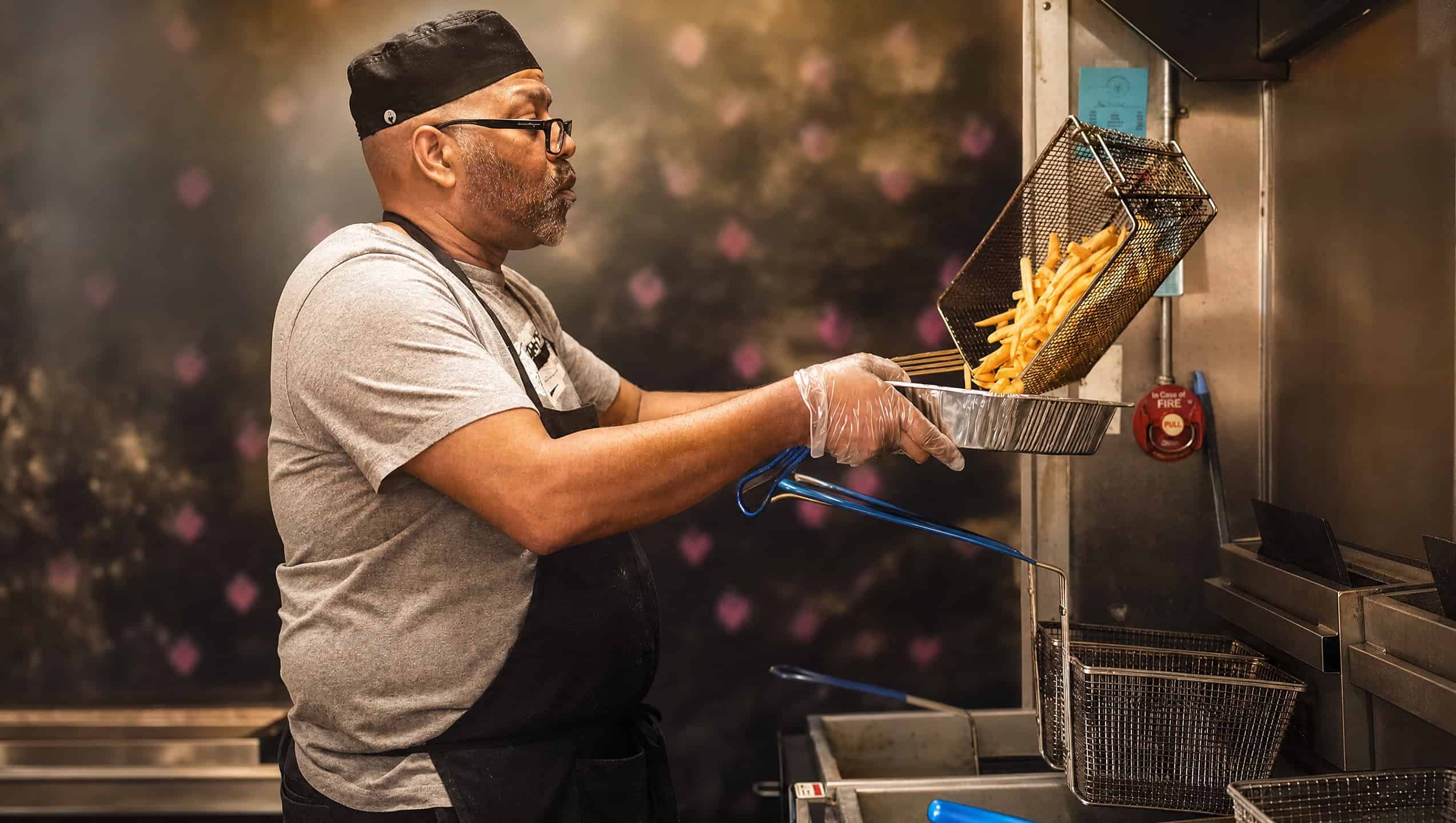 A cook at Pop's Soul Food lifting a basket of freshly fried golden fries over the fryer inside the food truck kitchen.